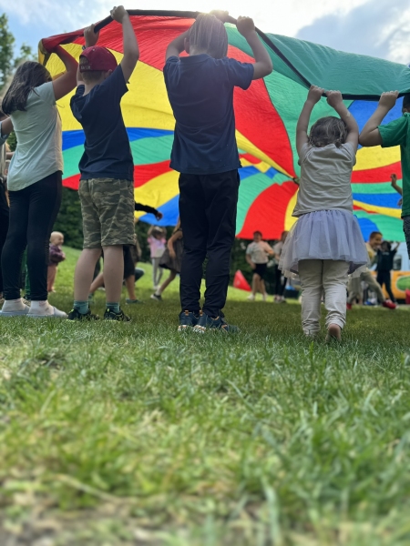 Zu sehen sind Kinder, die den bunten Fallschirm schwingen und ein Spiel spielen.