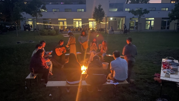 Eine Gruppe von Menschen sitzt um ein Feuer, lacht und unterhält sich, während die Flammen sanft lodern.